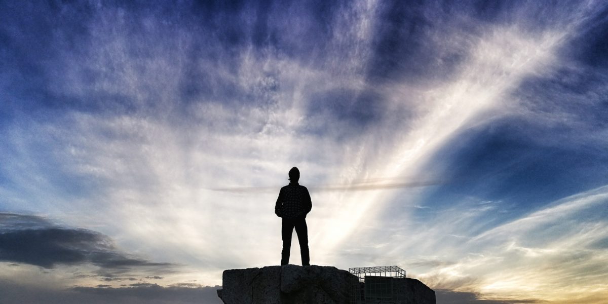 man looking to a sky on a cliff contemplate leadership qualities